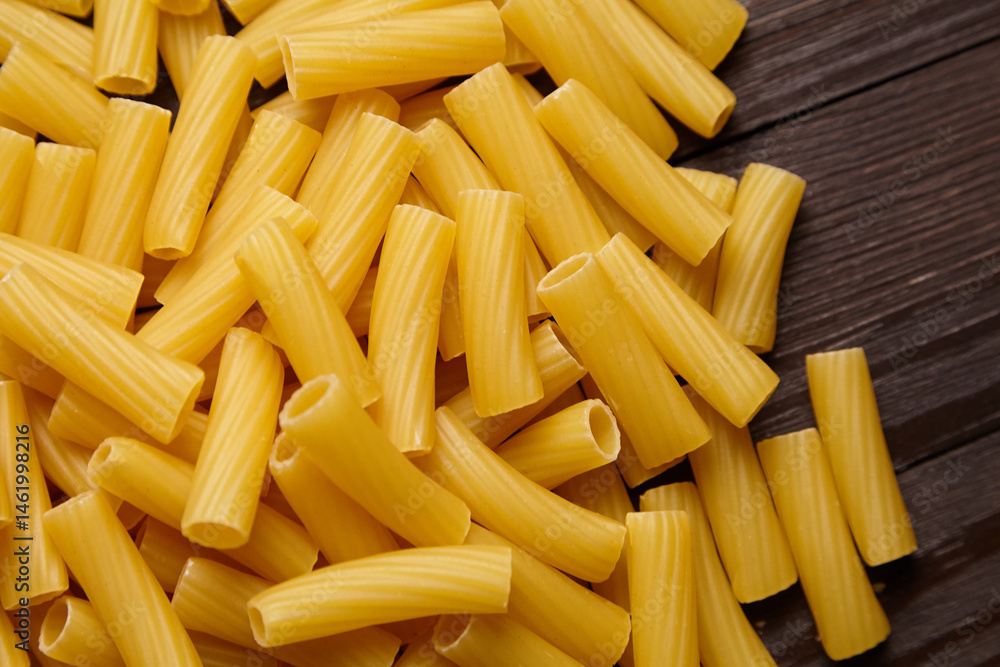 Close-up view of dry yellow tortiglioni pasta with ridged texture scattered over a dark wooden background Close-up view of dry yellow tortiglioni pasta with ridged texture scattered over a dark wooden background