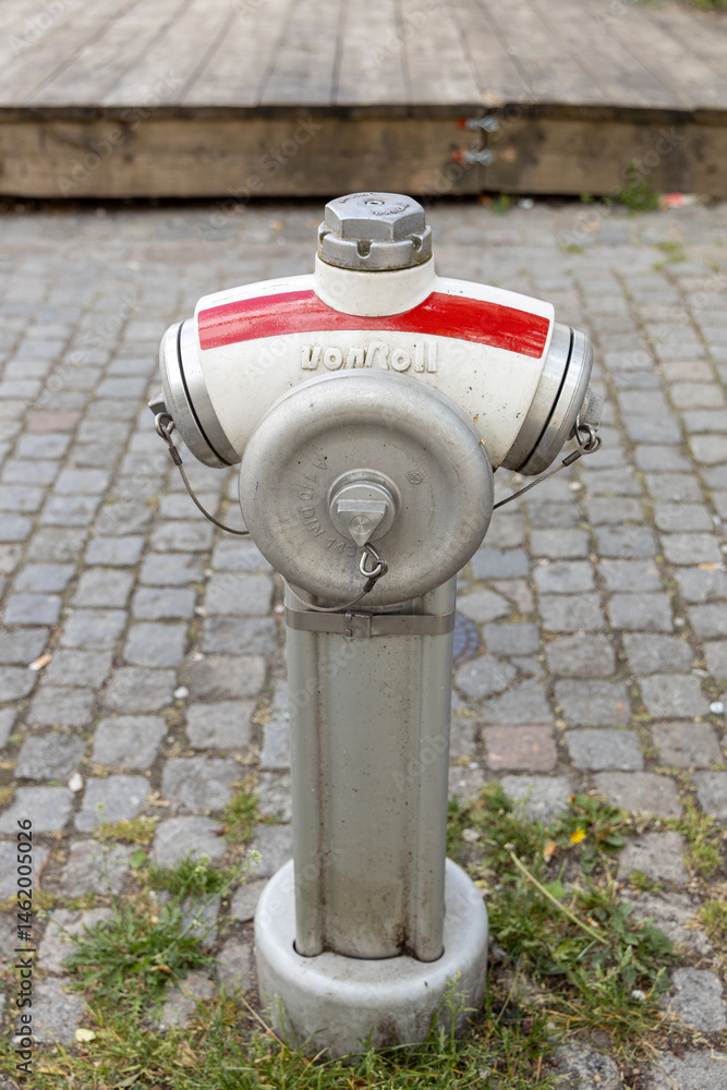 Fototapeta premium Fire hydrant with red and white color scheme stands on cobblestone street, showcasing urban infrastructure and public safety features