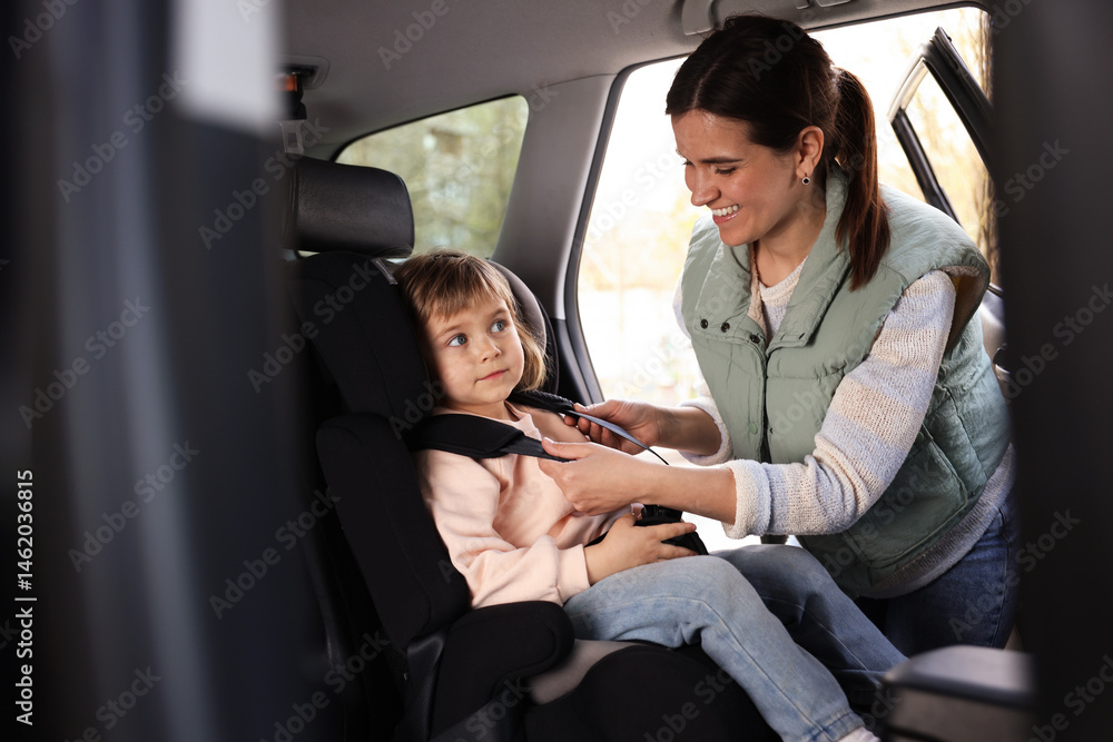 Fototapeta premium Happy mother fastening her daughter in child safety seat inside car