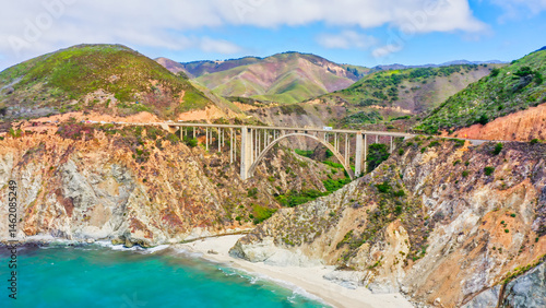 A stunning view of the iconic Bixby Creek Bridge on California Highway 1. The bridge stretches over picturesque cliffs and turquoise Pacific waters, creating a unique landscape and travel atmosphere.