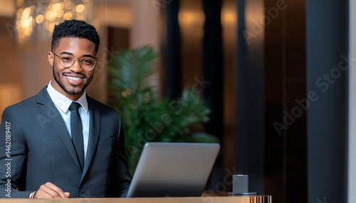 Obraz na płótnie A professional man in a suit smiles warmly while standing at a reception desk, conveying a welcoming and friendly atmosphere in a modern office environment. w salonie
