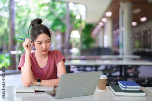 Free Download Young Asian Woman Studying Online with Laptop in Library Learning Education and Taking Notes in Notebook for Exam - GFXLoad