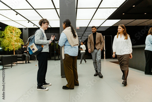 A group of adults from diverse backgrounds walk and talk in a modern office lobby near the entrance, including a woman and a man in businesswear.