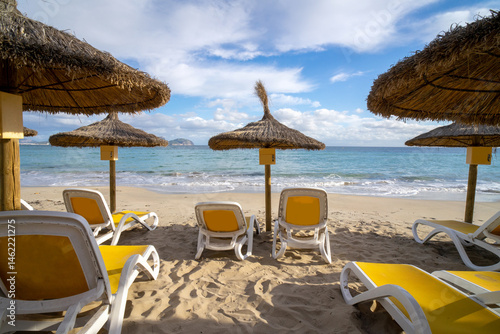 Fototapeta Naklejka Na Ścianę i Meble -  Umbrellas on the beach on the island of Majorca or Mallorca in the Balearic Sea,  part of Spain. Island in the Mediterranean Sea. Holidays by the sea, clouds, seascape. View of the sea and the island 