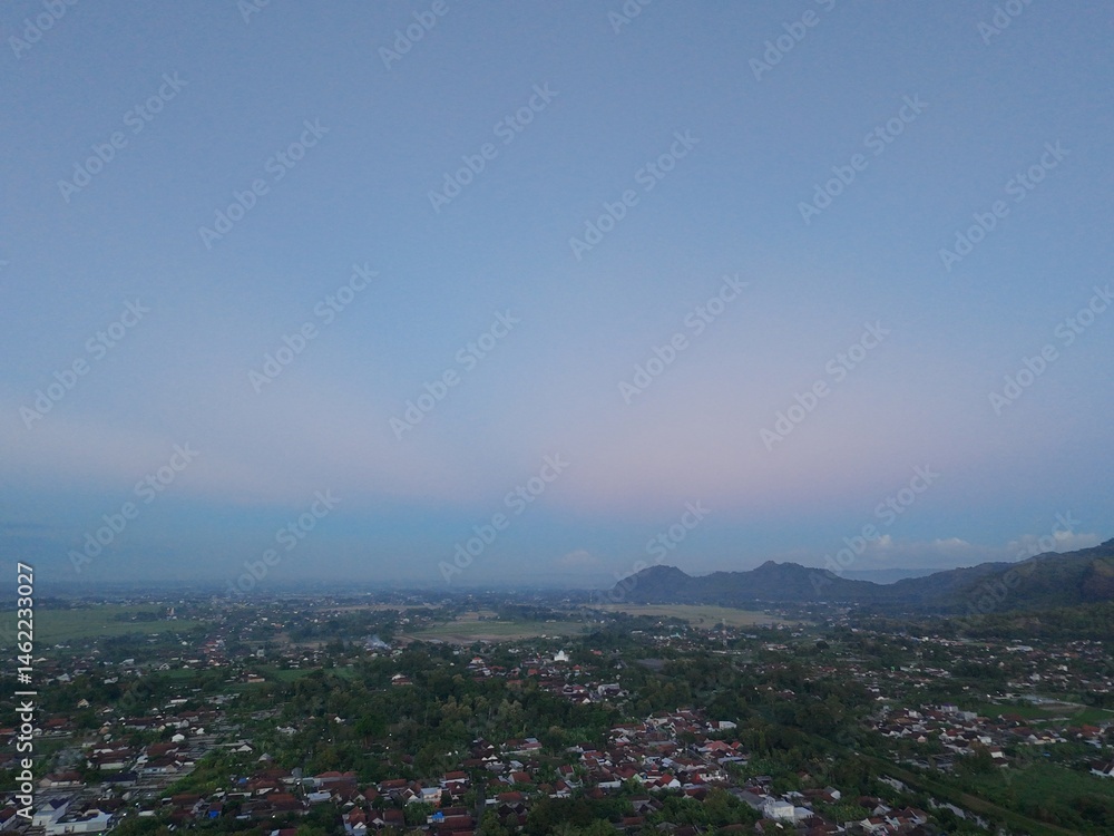 Obraz premium Aerial photography of rural settlement rice field scenery, bright blue sky in the afternoon sunset, clean white clouds with orange gradation