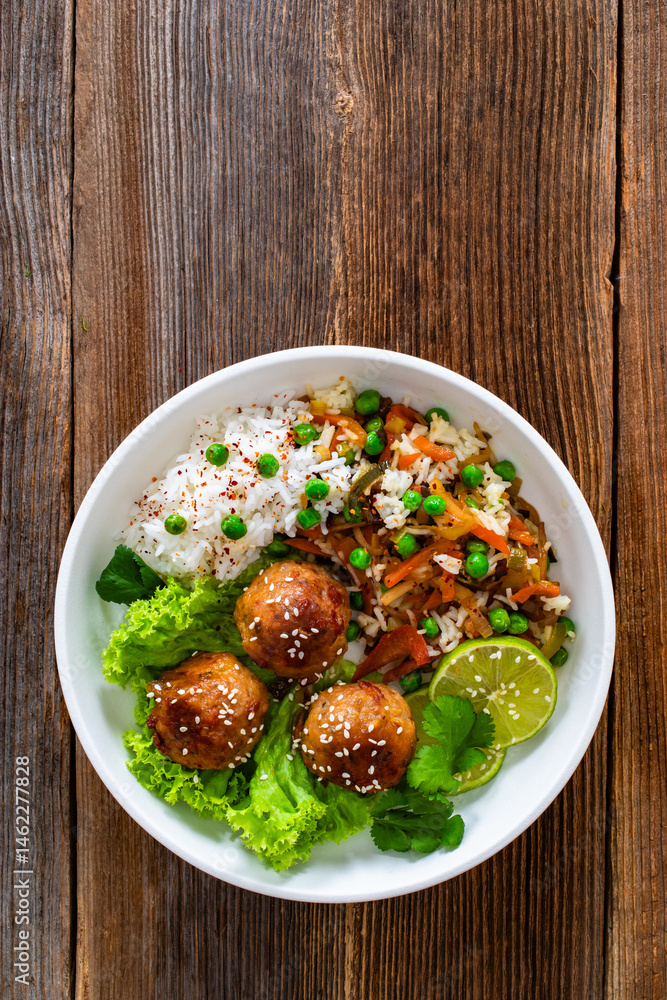 Asian style fried meatballs with mixed vegetables served with white rice on wooden background Asian style fried meatballs with mixed vegetables served with white rice on wooden background