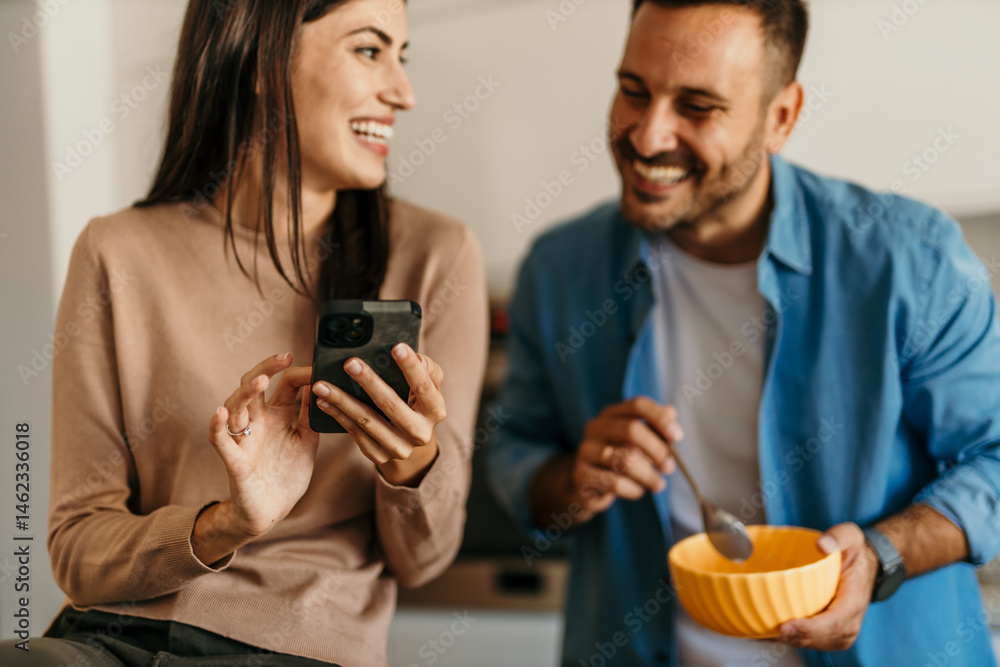 Cheerful couple enjoying breakfast and social media in modern kitchen Cheerful couple enjoying breakfast and social media in modern kitchen
