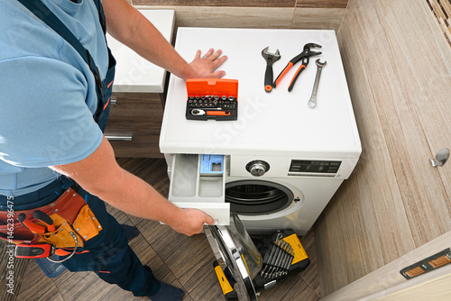 Repairman opening the detergent drawer of a washing machine during maintenance, with tools on top of the appliance