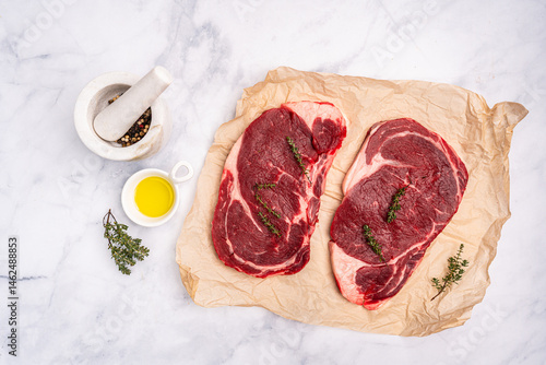 Obraz na płótnie Raw fresh beef steak on a paper with spices on a white background. Top view with copy space. High quality photo w salonie