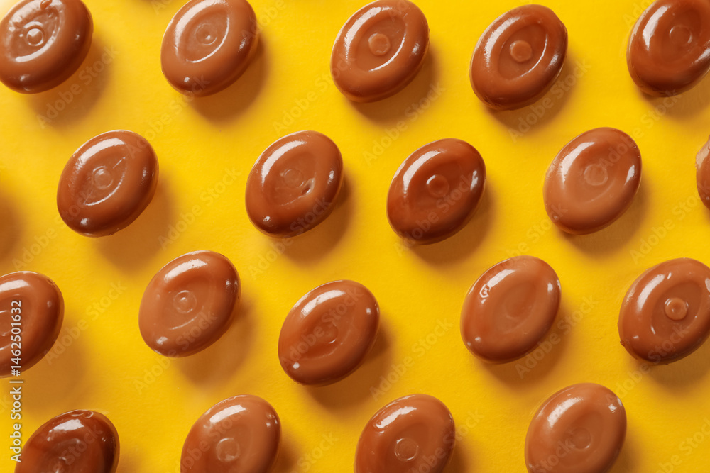 Fototapeta premium Many tasty caramel candies on yellow background, flat lay