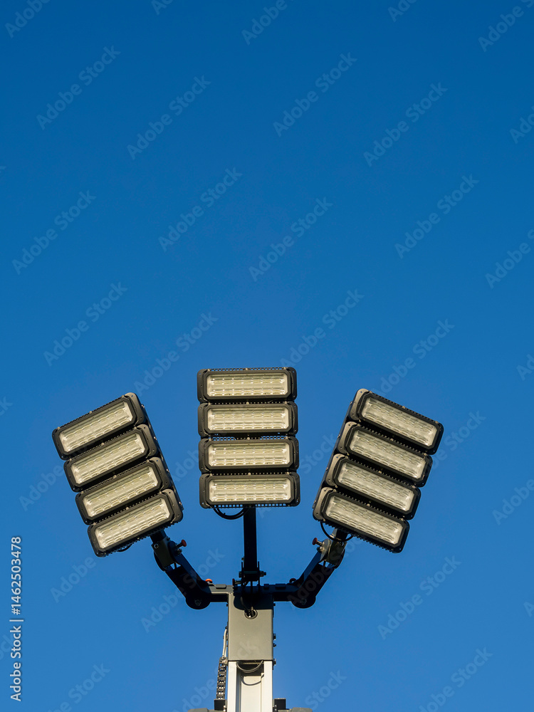 Powerful mobile LED panels on a tall metal pole for sport event illumination or a concert. Blue cloudy sky background. Modern efficient technology. Floodlight ready for work.