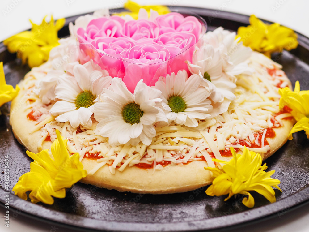 Pink roses in heart love shape and white chamomile flowers on top of a pizza and on dark metal cooking round tray and on white background. Abstract conceptual art. Selective focus.