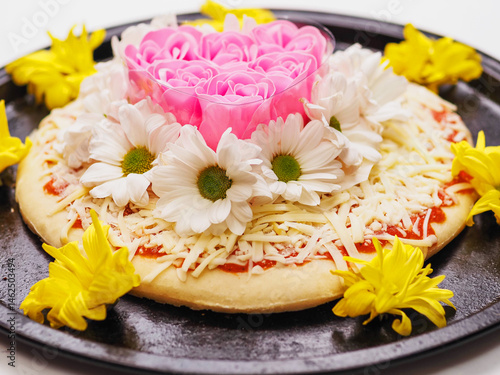 Obraz na płótnie Pink roses in heart love shape and white chamomile flowers on top of a pizza and on dark metal cooking round tray and on white background. Abstract conceptual art. Selective focus. w salonie
