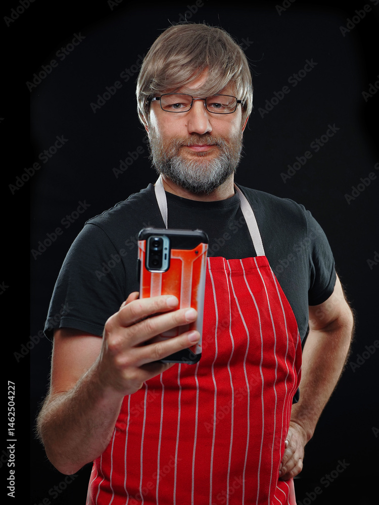 Male butcher or fish monger in black shirt and classic red and white stripe apron. Dark background. Strong edge lighting on the subject. Model in his 40s or 50s with grey beard and slim athletic body.