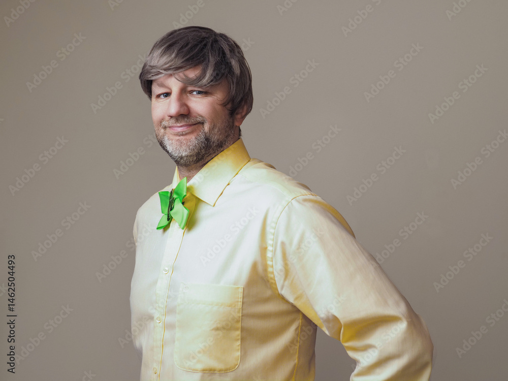 Man in yellow shirt and green bow with shamrock on light color background. Irish sport supporter or fan. Model in his 40s or 50s with grey beard and hair.