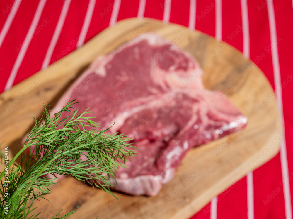 Fresh uncooked T bone steak with fresh dill and garlic cloves on wooden cutting board and on classic red and white stripe table cloth. High quality beef meat product. Butcher craft.