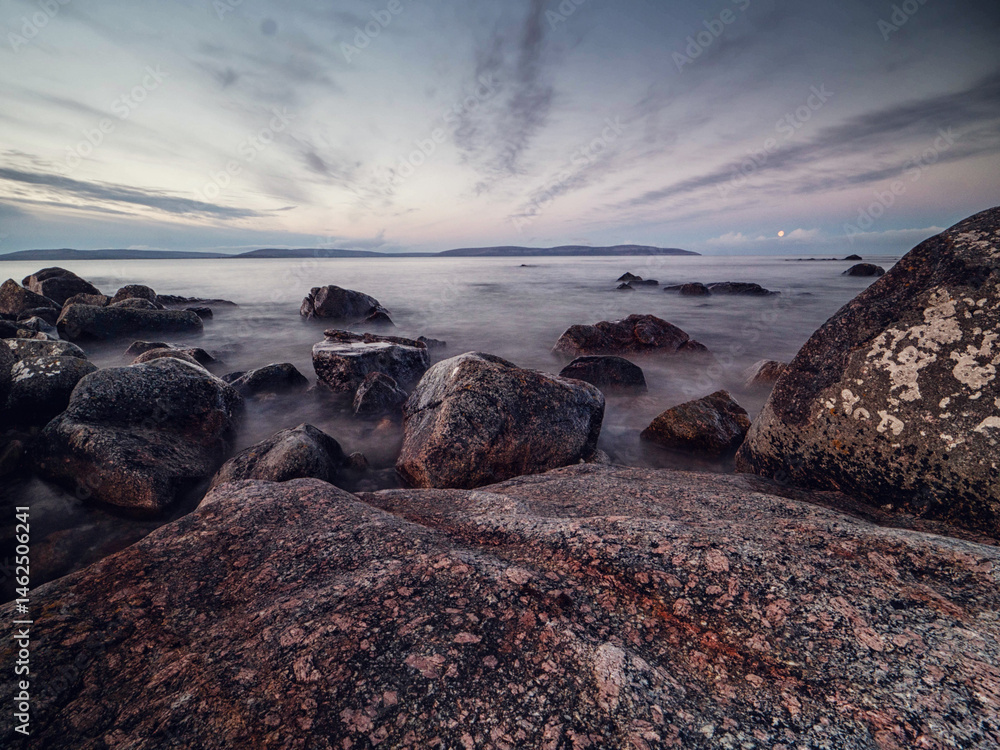 View on peaceful Galway bay and Burren mountains from rough stone coast. Water surface is smooth and gives relaxing feel and mood. Irish nature landscape scene. Nobody. Cloudy sky.