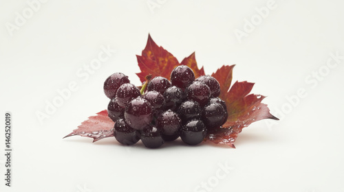 A small cluster of red table grapes, adorned with dewy droplets and grape leaves, stands out against a white background