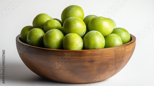 Obraz na płótnie A wooden bowl filled with crisp, unripe green plums sits against a white backdrop w salonie