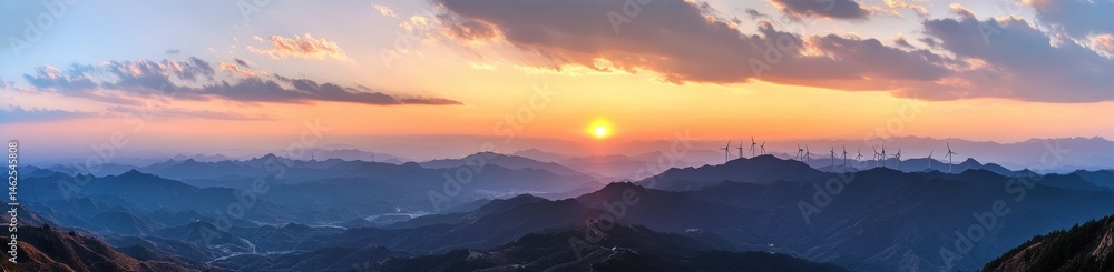 Fototapeta premium Sunrise over a mountain range, with hazy valleys and wind turbines visible on the horizon
