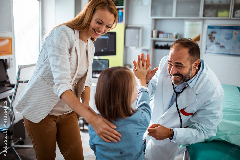 Smiling doctor using stethoscope to check young girl at medical clinic with mother nearby Smiling doctor using stethoscope to check young girl at medical clinic with mother nearby