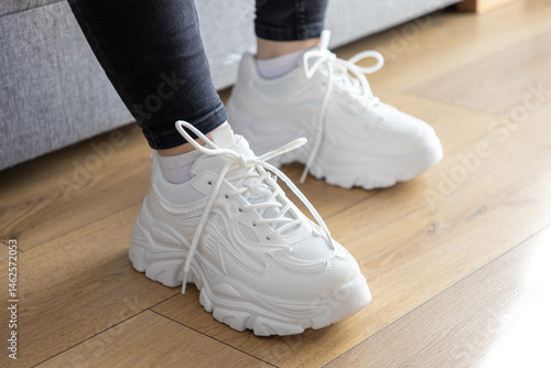 Tableau sur toile White chunky sole sneakers with laces and worn appearance on wooden floor, illus