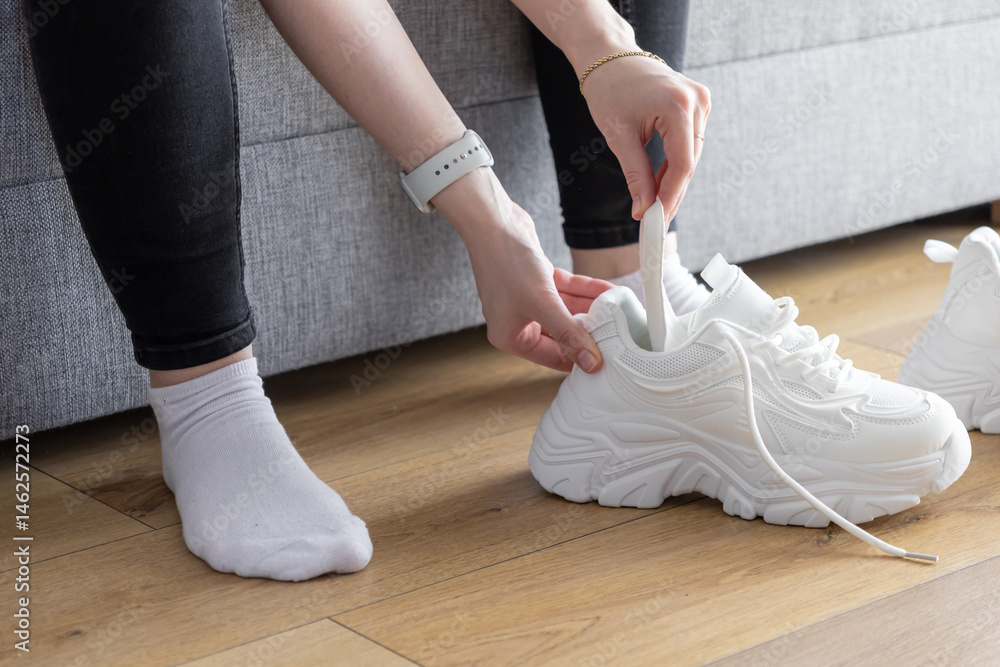 Fototapeta premium Person's hands inserting white shoe shaper into athletic training sneaker indoors, maintaining shape and freshness for next use