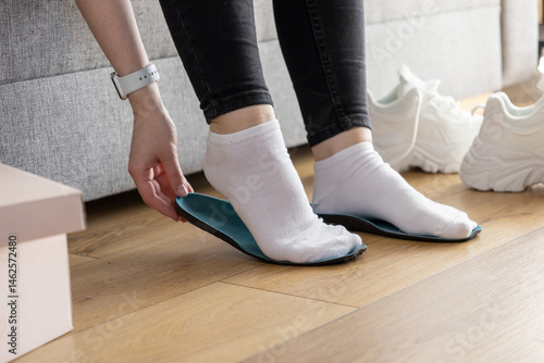 Fotografi Person's hands placing blue insole onto socked foot indoors, preparing for comfo