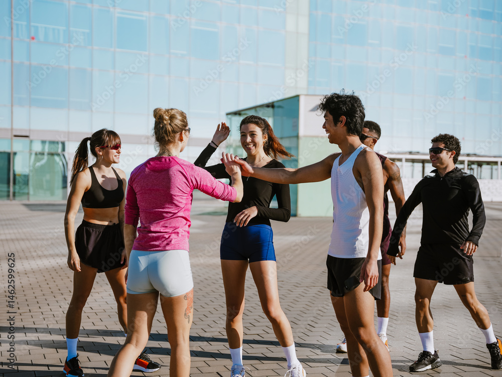 Fototapeta premium A group of six athletes laugh and talk while about to give each other a high five, outdoors