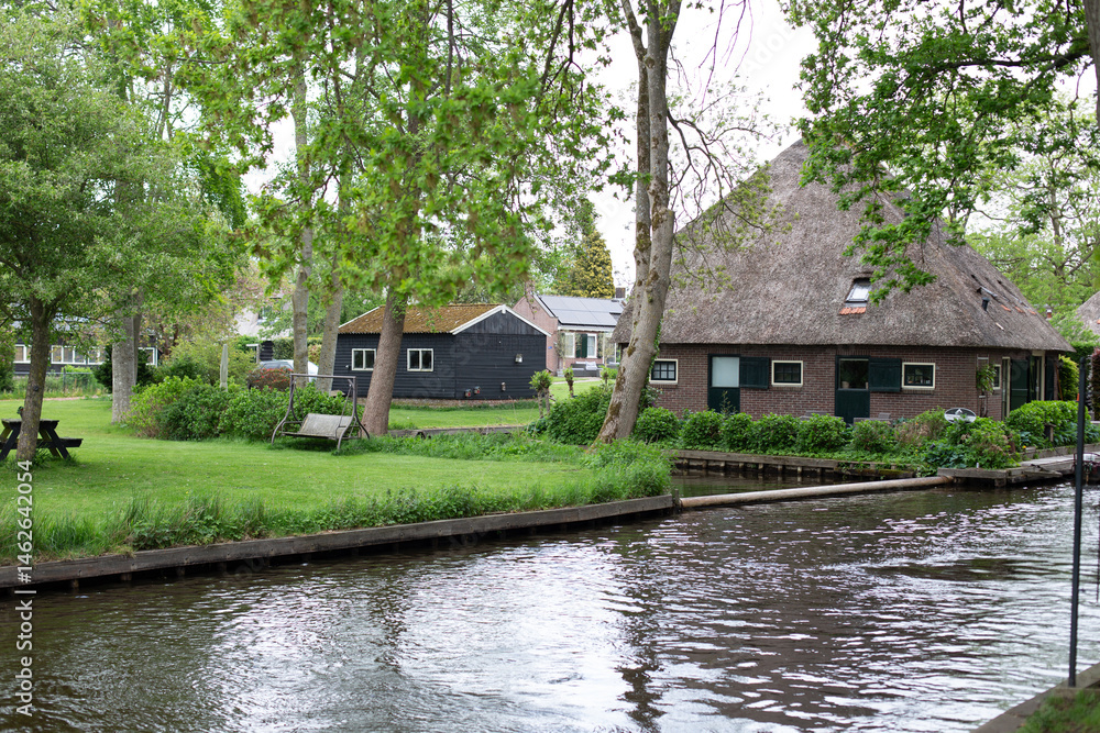 Obraz premium Giethoorn, Netherlands – A picturesque village with canals and rustic thatched-roof houses in a scenic farm area on a warm spring day in Europe.