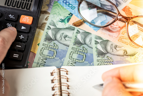 Costa Rica money, financial analysis, company accounting, tax calculation, financial business concept. Costa Rican colones together with a calculator, hand writing down the results in a notebook