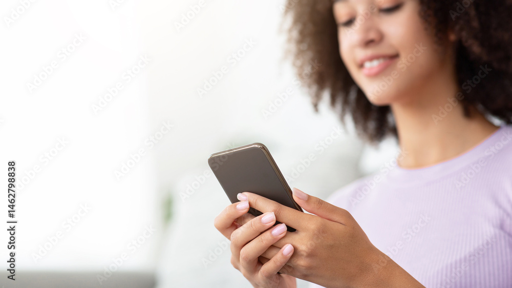 Modern online communication during covid-19 lockdown, home alone, new normal, be safe. Cheerful young african american woman typing message or surfing on phone in living room interior, selective focus Modern online communication during covid-19 lockdown, home alone, new normal, be safe. Cheerful young african american woman typing message or surfing on phone in living room interior, selective focus