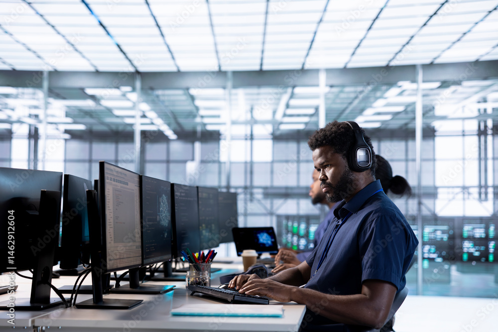 Engineer in data center listening music while using PC to check for server performance issues arising due to high CPU usage. Man wearing headphones in server farm fixing insufficient memory errors