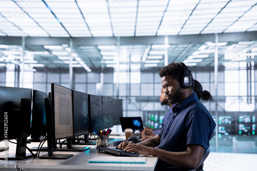 Obraz na płótnie Engineer in data center listening music while using PC to check for server performance issues arising due to high CPU usage. Man wearing headphones in server farm fixing insufficient memory errors w salonie