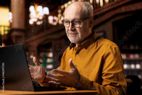 Obraz na płótnie Senior man involved in a remote classroom experience via online platform, using wireless internet to study a university course and chatting with his teacher. Reviewing project materials. w salonie