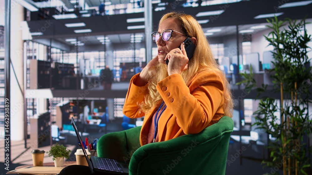 Determined businesswoman speaking on a phone call to ensure project development success, multitasking in a corporate office. Female CEO using remote connection on her smartphone. Camera B.