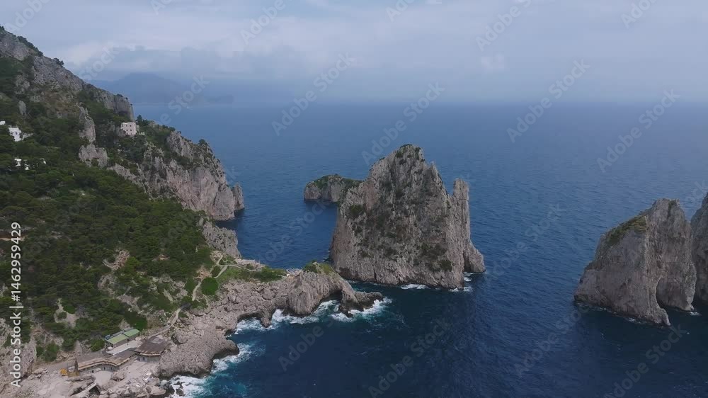 Aerial view of Capri, Italy, showcasing the Faraglioni rock formations, lush greenery, white cliffside buildings, and vibrant blue sea in motion. Aerial view of Capri, Italy, showcasing the Faraglioni rock formations, lush greenery, white cliffside buildings, and vibrant blue sea in motion.