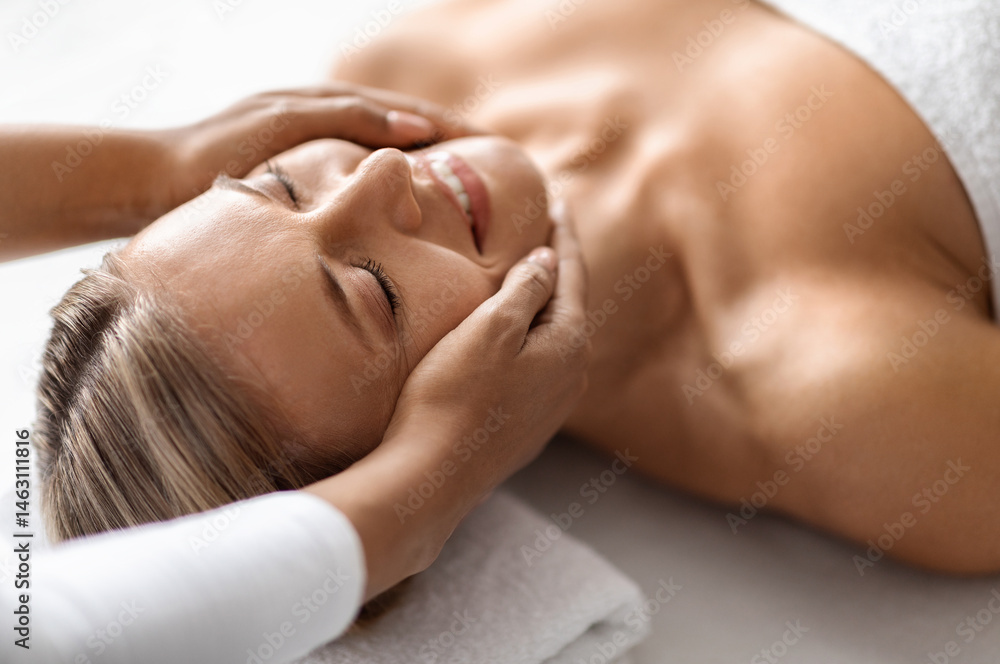 Beautiful middle aged woman enjoying face lifting massage in spa salon, professional therapist making skin lift procedure to relaxed mature female lying on table in wellness center, closeup Beautiful middle aged woman enjoying face lifting massage in spa salon, professional therapist making skin lift procedure to relaxed mature female lying on table in wellness center, closeup