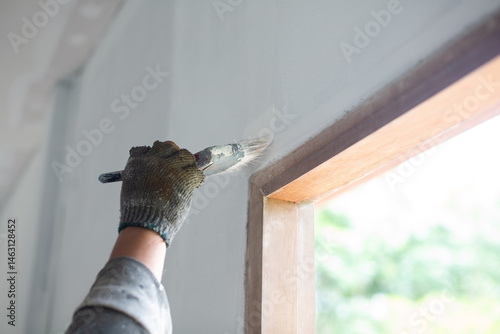 Painter's hands in cloth gloves holding a paintbrush on a white house wall.