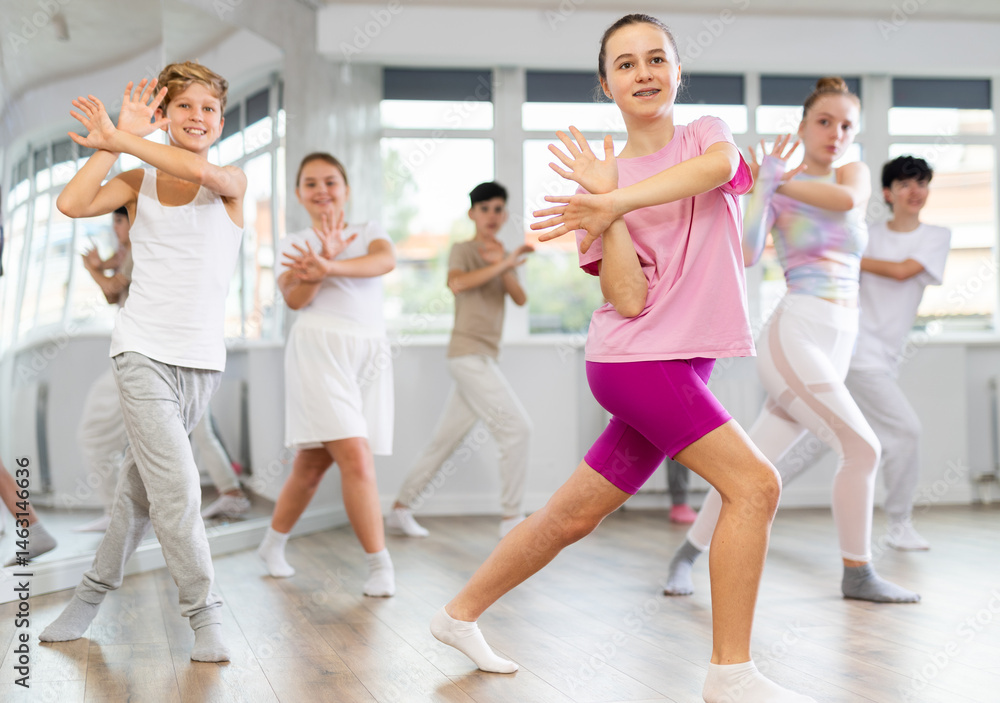 Naklejka premium Positive female teenager dances vogue in choreographic school, group of young people in sportswear trains together with their classmates in gym before competitions, battle