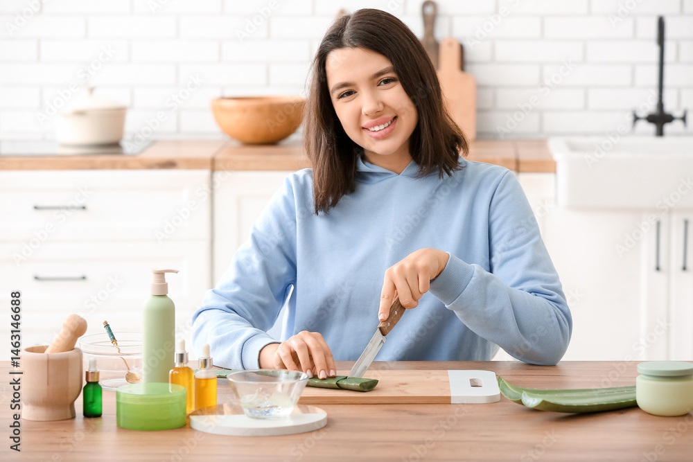 Happy young woman cutting aloe vera leaf for organic cosmetics near table in kitchen Happy young woman cutting aloe vera leaf for organic cosmetics near table in kitchen