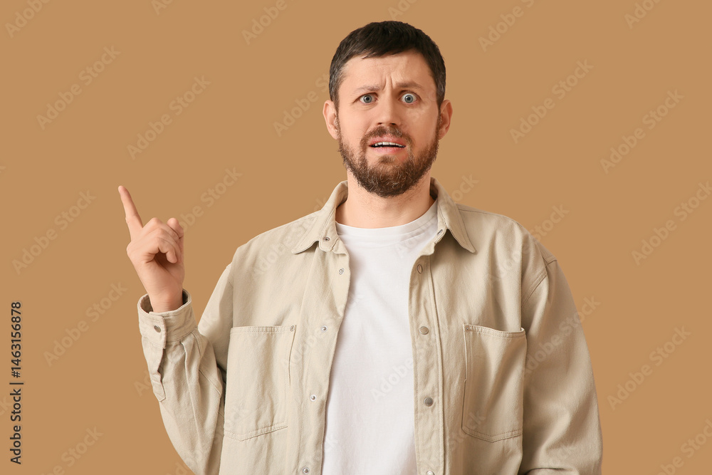 Shocked young man pointing at something on beige background Shocked young man pointing at something on beige background