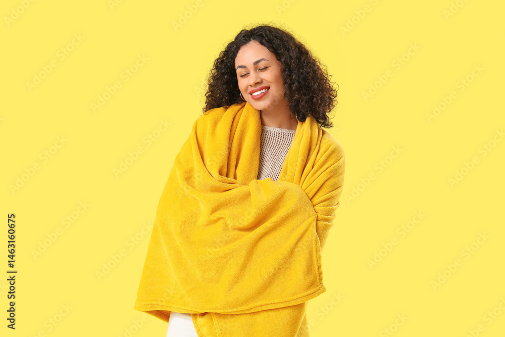 Fototapeta premium Beautiful young African-American woman with cozy blanket on yellow background