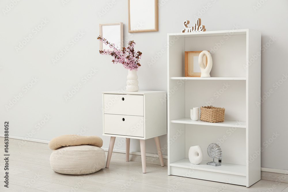 Fototapeta premium Dresser with shelving unit, different decor and vase of pink blooming branches near white wall in living room