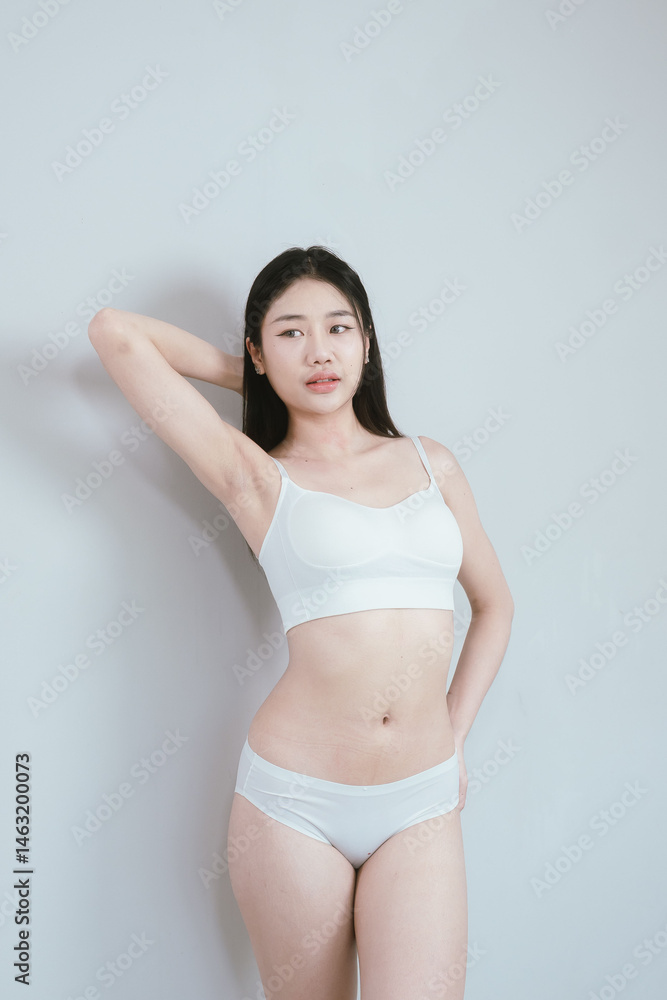 Obraz premium Attractive young woman in lingerie posing in studio, showcasing slim waist, smooth skin, fit figure, and healthy lifestyle emphasis