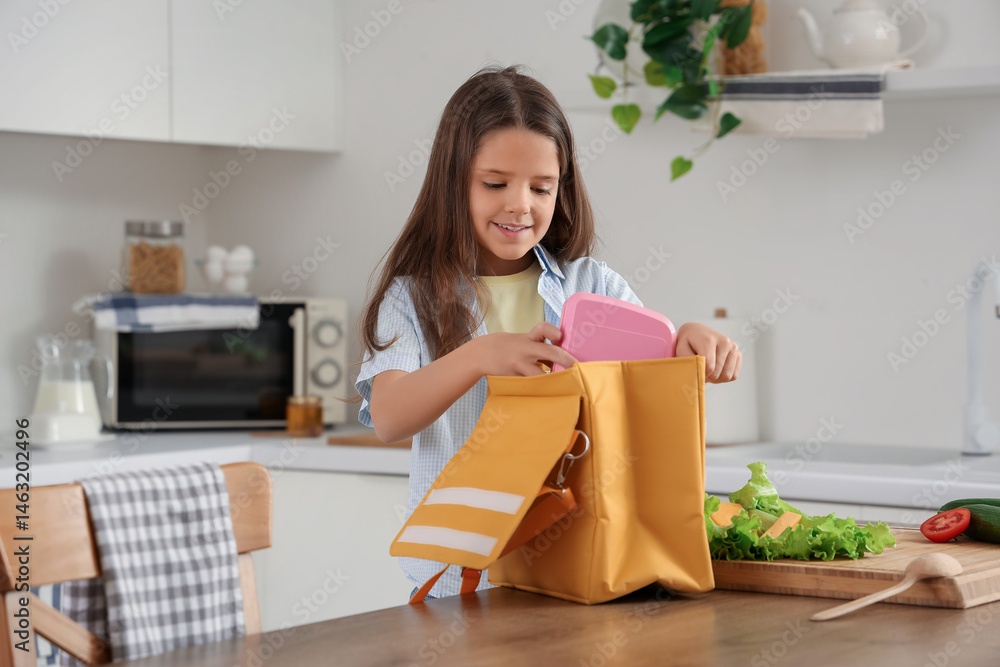 Cute girl packing school lunch box into bag in kitchen Cute girl packing school lunch box into bag in kitchen