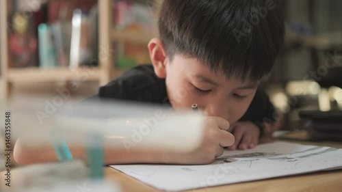 Asian boy about 7 years old drawing picture by pencil on white paper