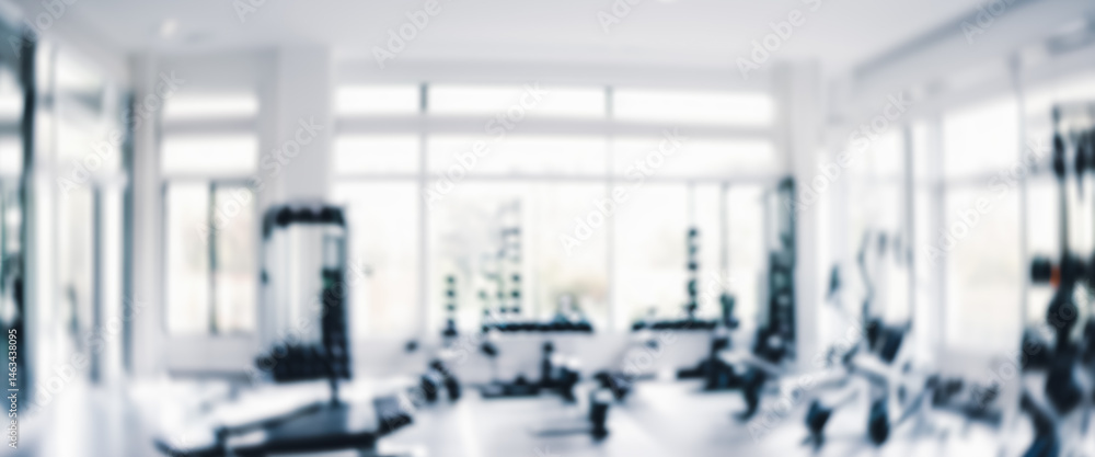 Blurred gym interior with exercise equipment and large windows in a bright setting. Blurred gym interior with exercise equipment and large windows in a bright setting.
