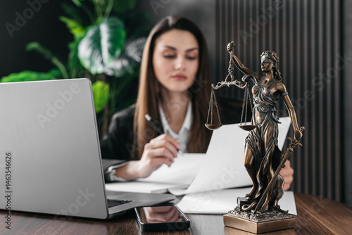 Obraz na płótnie A female lawyer works on a laptop with scales of justice on a courtroom table