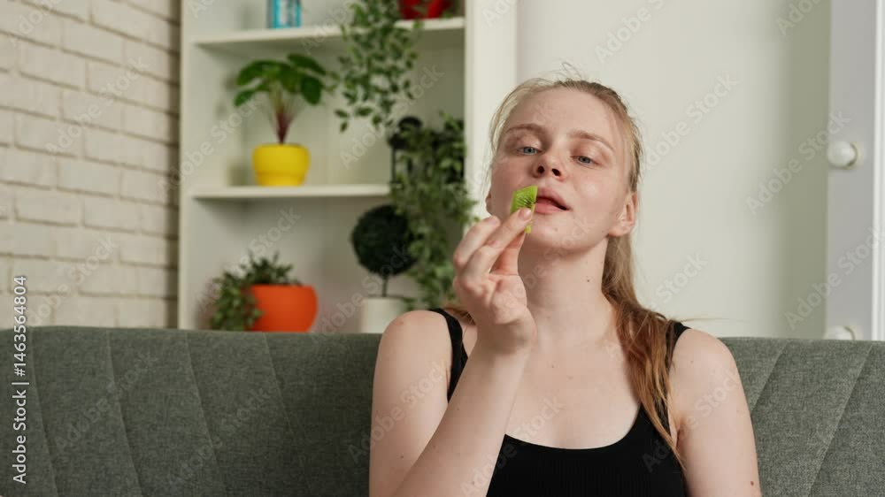 Young woman sitting on sofa at home and eating fresh vitamin fruit, biting ripe kiwi slices, chewing and smiling, enjoying snack. Slow motion. Young woman sitting on sofa at home and eating fresh vitamin fruit, biting ripe kiwi slices, chewing and smiling, enjoying snack. Slow motion.